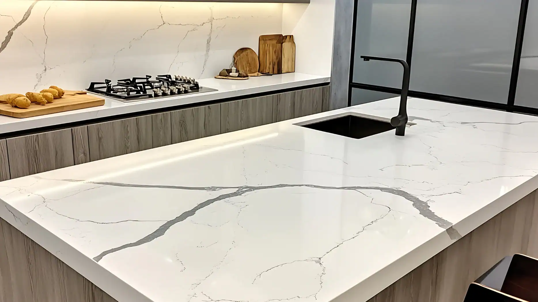 A modern NY kitchen with a white marble countertop featuring gray veining, an inset black sink with a black faucet, a gas stove, wooden cutting boards, and fresh bread—ideal for showcasing marble restoration Nassau & Suffolk County services.