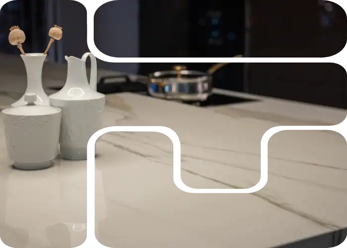 A modern kitchen countertop with a white marble surface, featuring two white ceramic vases and a stainless steel pan in the background. The countertop has visible gray veining, showcasing the quality of marble restoration Nassau & Suffolk County, NY offers.