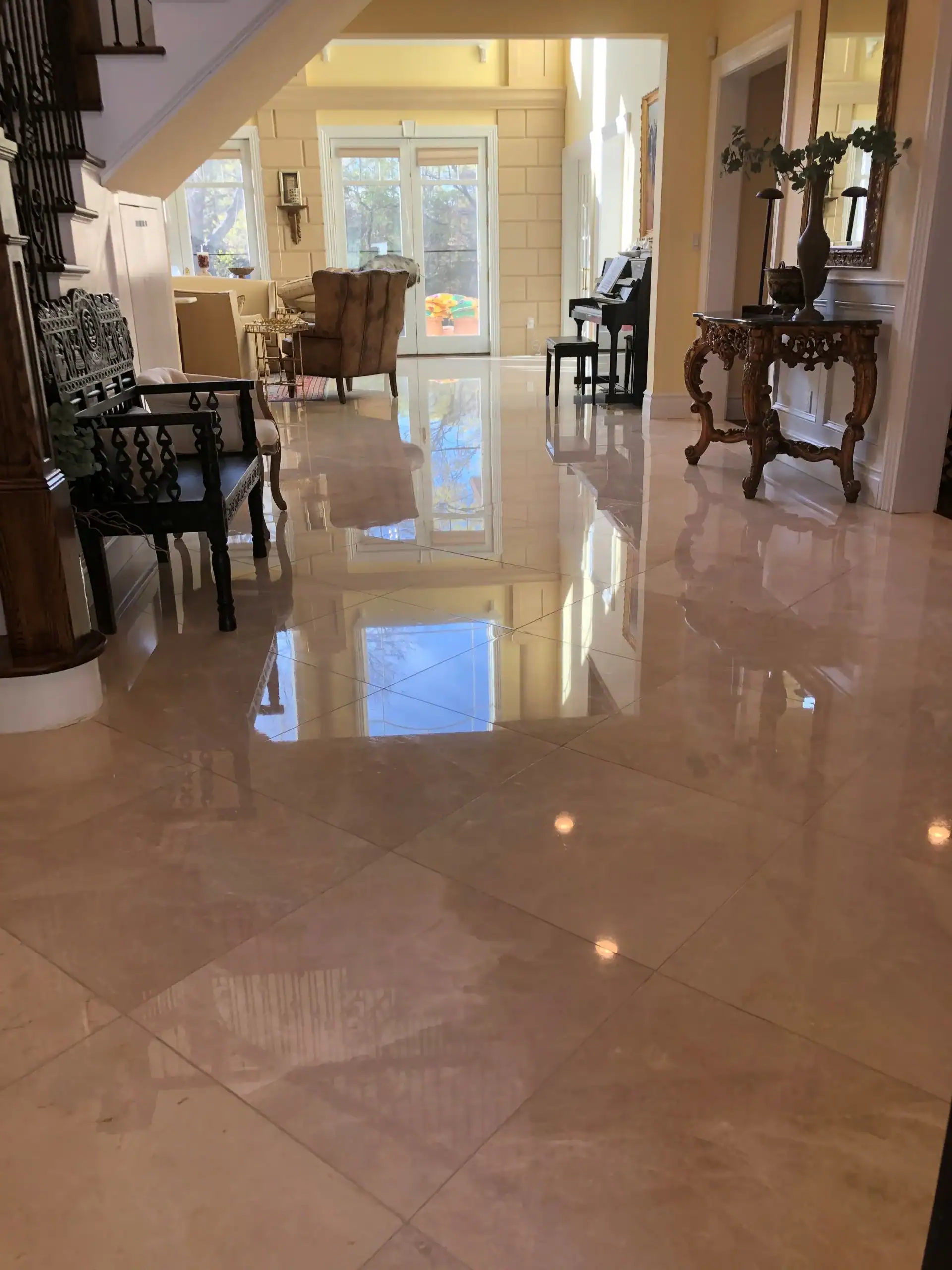 A spacious, elegant hallway in NY with glossy marble floors—restored by marble restoration Nassau & Suffolk County—reflecting light, classic wooden furniture along the walls, and large windows at the far end letting in natural sunlight.