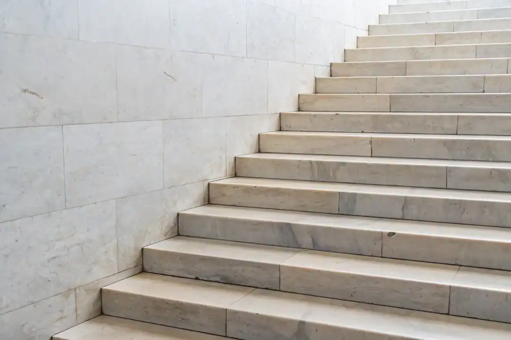 A close-up view of white marble stairs ascending alongside a smooth marble wall, with even lighting highlighting the clean, modern design.
